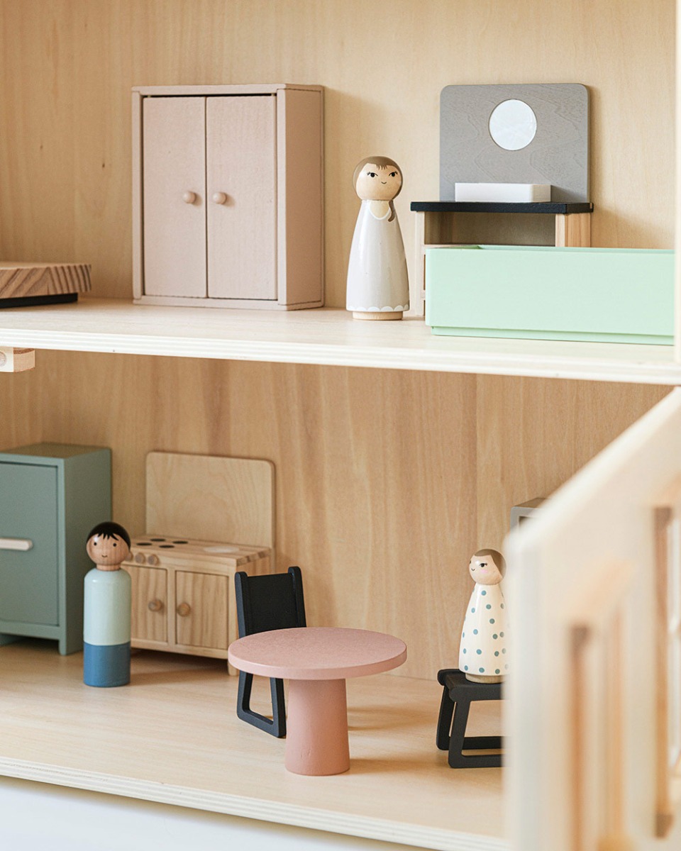 Intérieur de maison de poupée en bois avec meubles miniatures et figurines en bois, comprenant table, chaises, armoire et kitchenette, dans des tons doux et naturels.